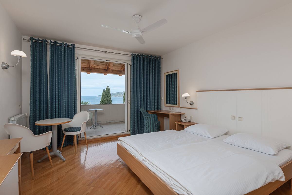 Une chambre d’hôtel comprenant un lit, un bureau, une chaise, une petite table et donnant sur l’extérieur.