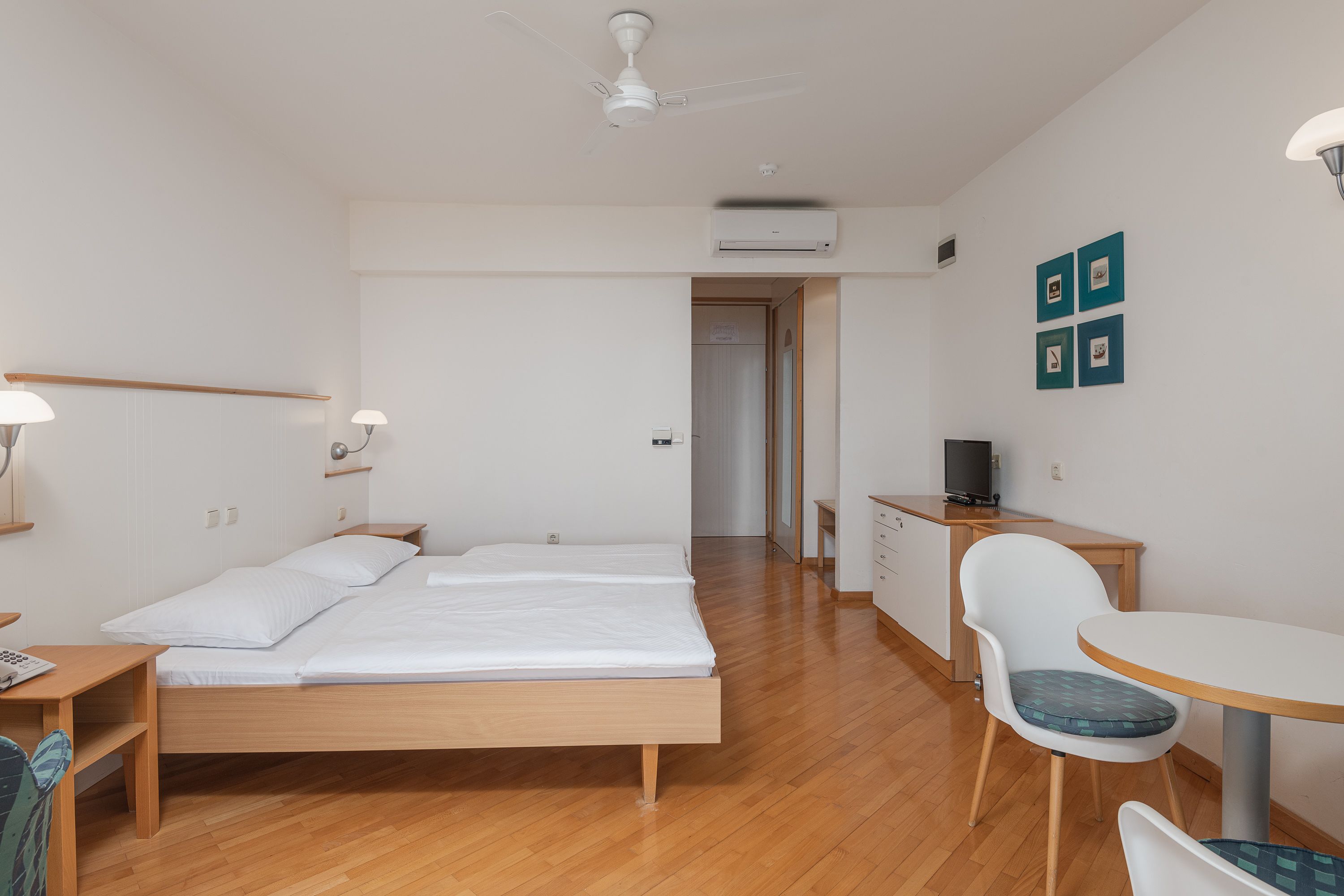 Une chambre d’hôtel avec un lit en bois, un bureau, une chaise et une petite table.