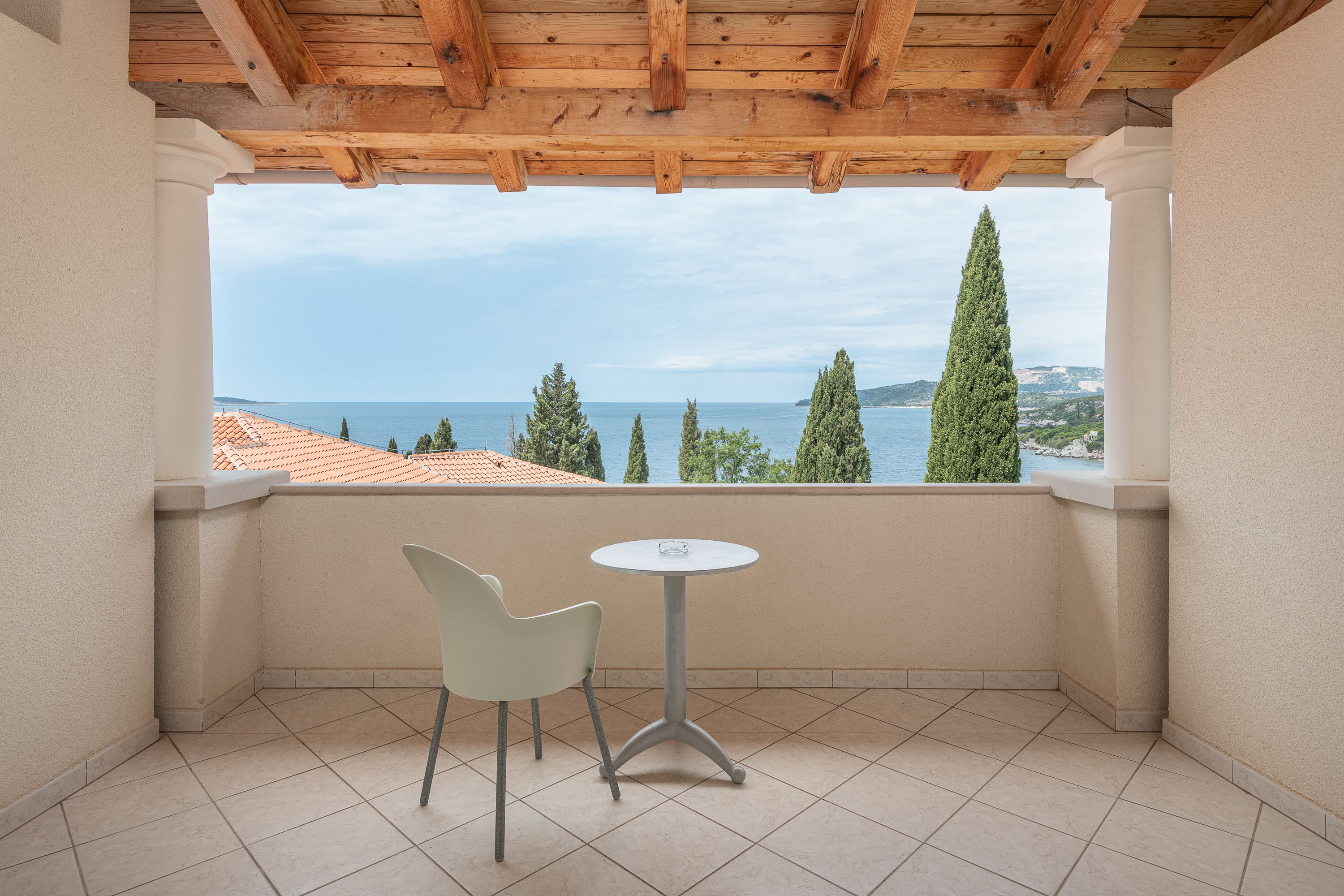 A balcony with a view of the sea, a table, and a chair.