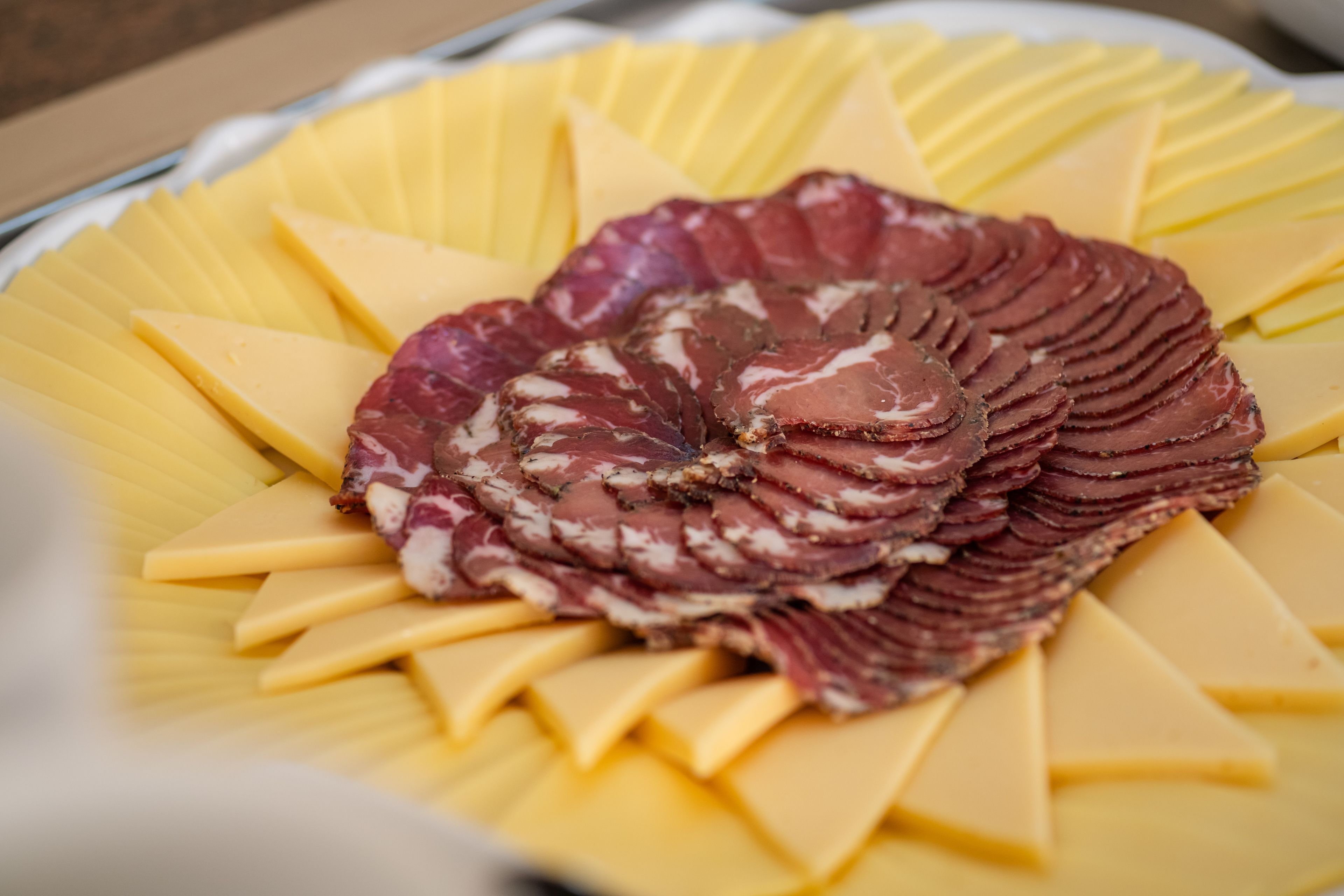 Une assiette de charcuteries et de fromages coupés en tranches, disposés en forme d’éventail.