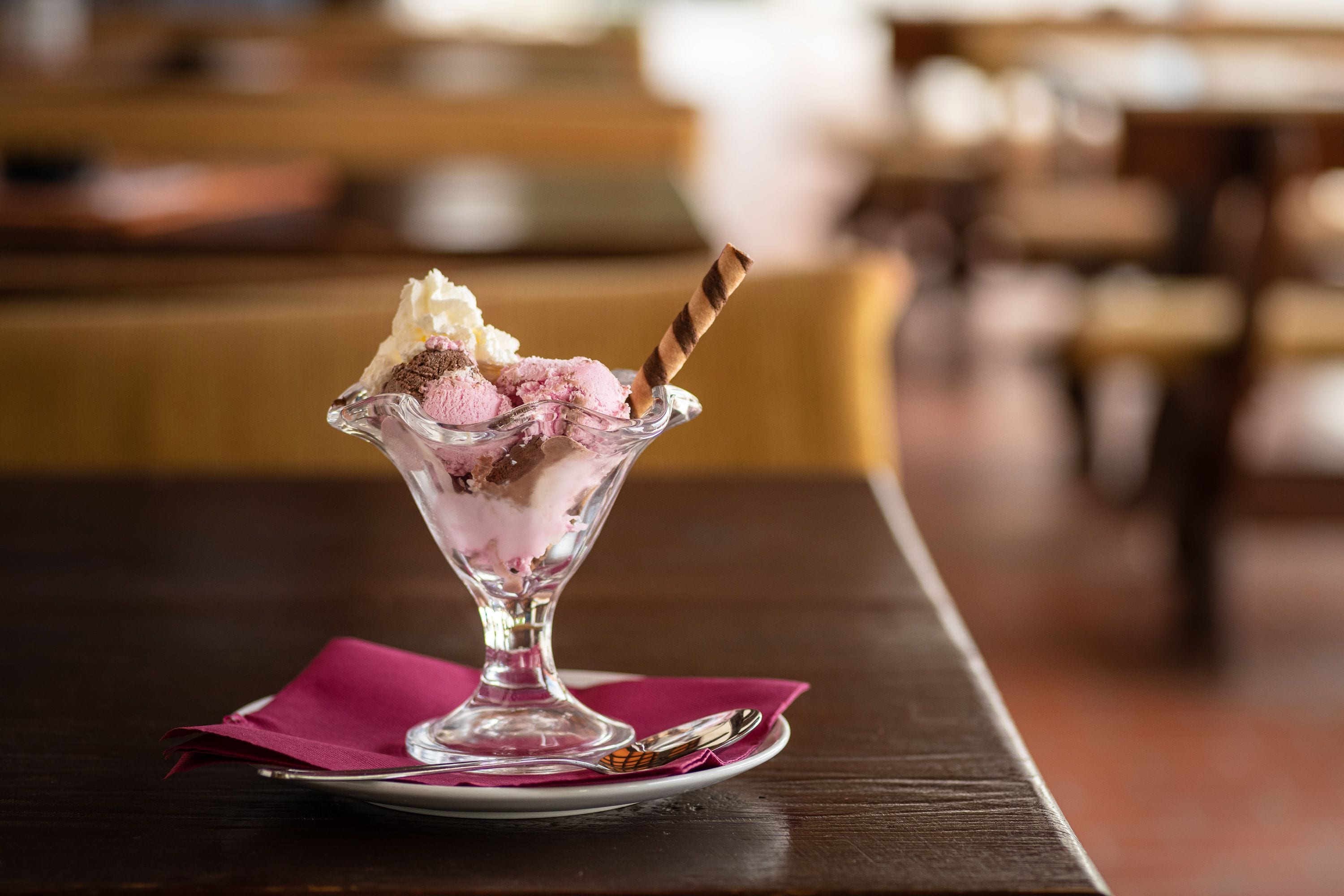 A dessert in a glass bowl on a table with a pink napkin and a spoon.