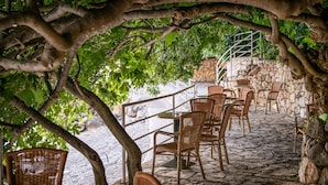 An outdoor patio with wicker chairs and tables, surrounded by stone walls and a stone staircase.