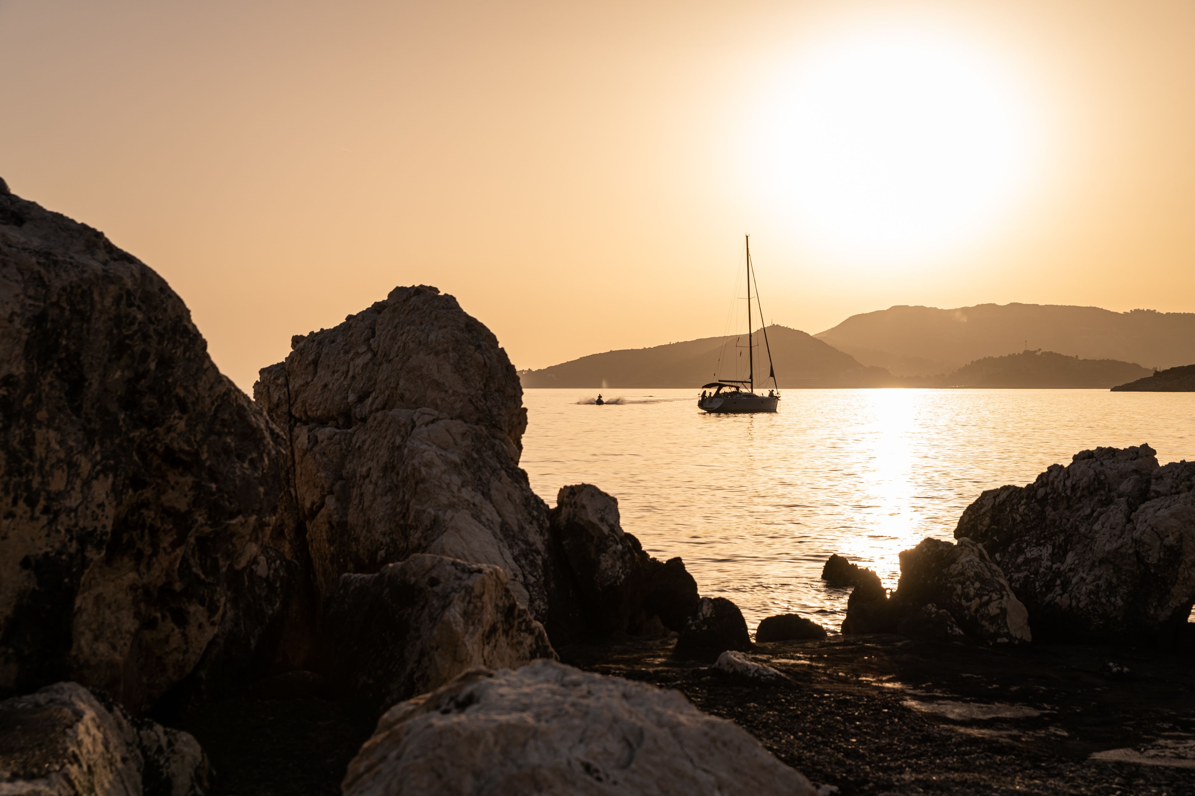 A rocky shoreline with a sailboat on calm waters, under a clear sky.