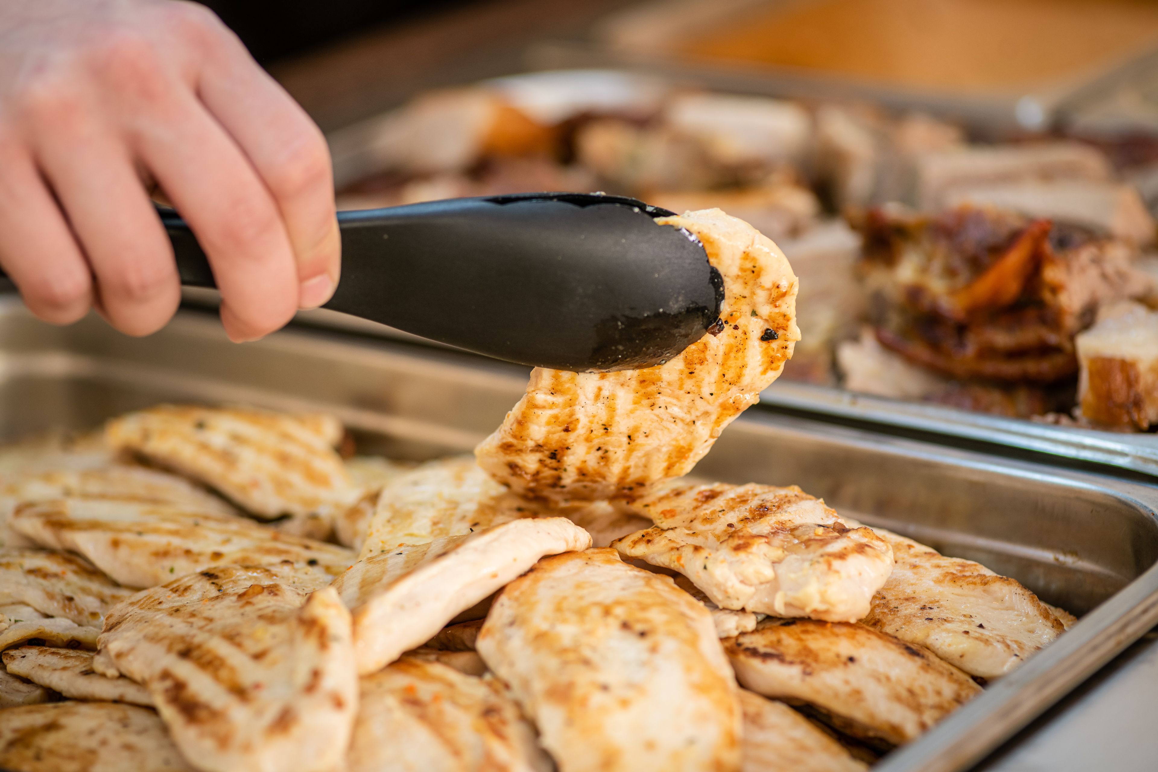 A hand using tongs to serve grilled chicken wings from a buffet tray.