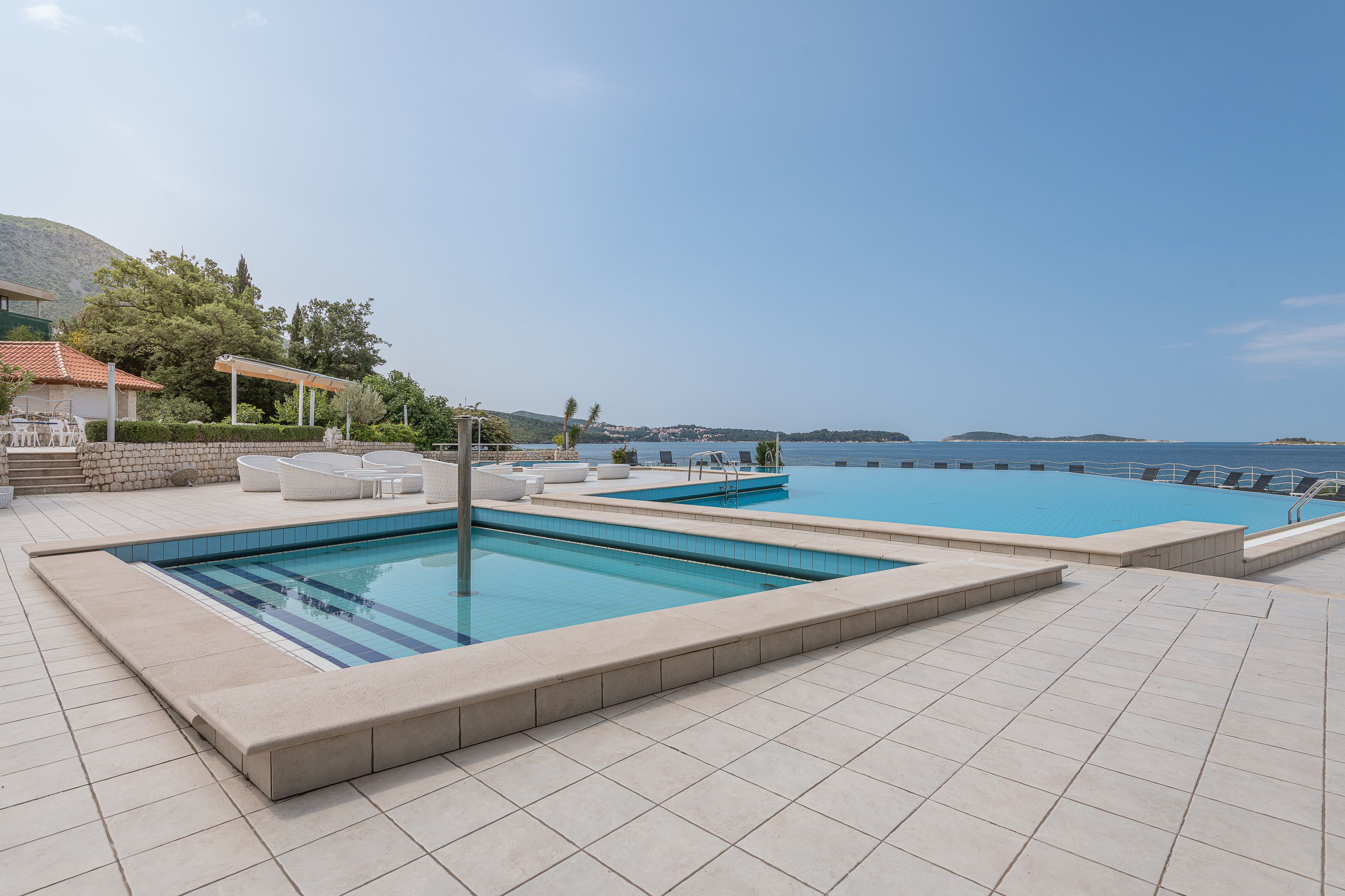 Un área de piscina con varias piscinas, una zona de estar cubierta y vistas al mar.