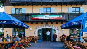 Un área de comedor al aire libre con mesas de madera y sombrillas azules con el rótulo "PAULANER".