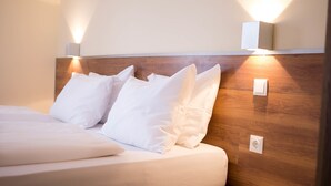 Una cama bien hecha con sábanas y almohadas blancas, cabecera de madera y una lámpara fijada a la pared.
