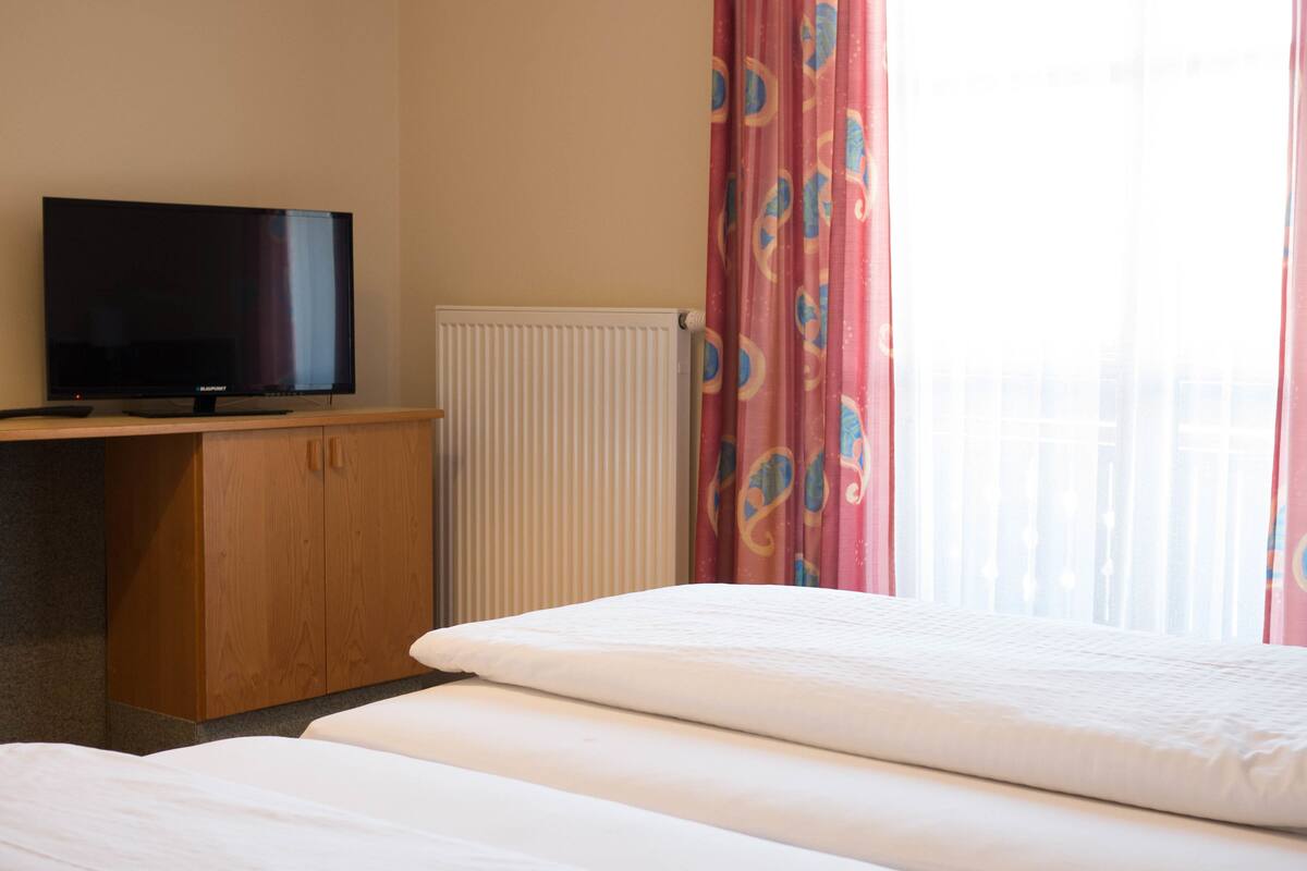 A hotel room with a bed, a television on a wooden cabinet, and a window with pink curtains.