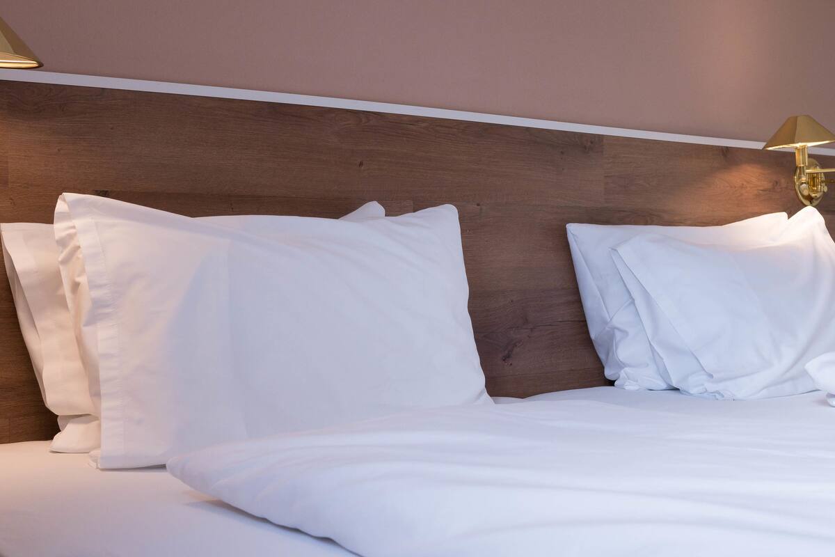 A hotel room with a wooden headboard, white bedding, and two bedside lamps.