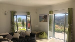 A living room with a black leather sofa, a green bean bag, and a view of a mountainous landscape through large sliding glass doors.