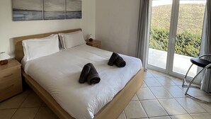 A bedroom with a bed, a nightstand, a lamp, a chair, and a view of the outdoors.