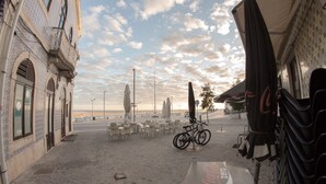 Un café situé en bord de mer, avec des tables à l’extérieur, un vélo et une enseigne Coca-Cola Zero.