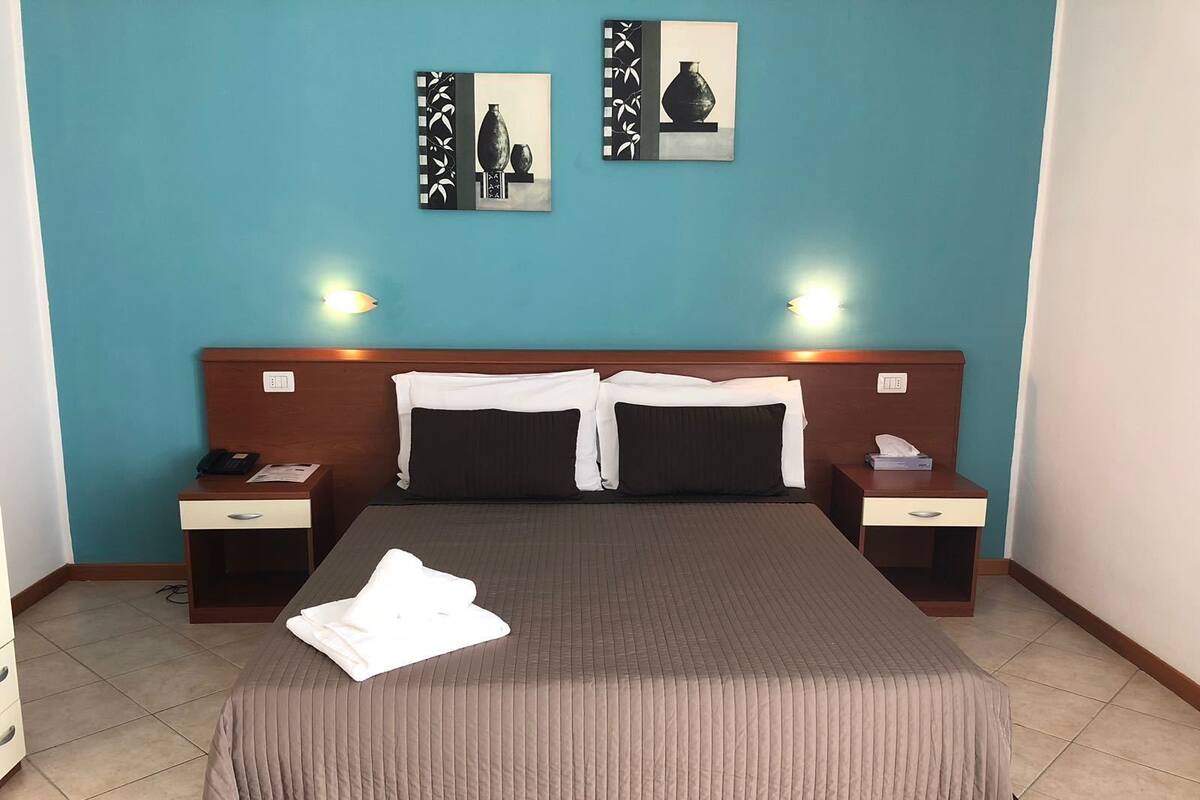 Una habitación de hotel con una cama grande, dos mesitas de noche y dos lámparas de pared.