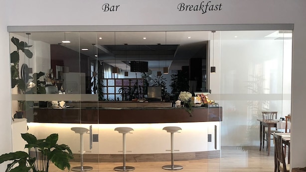 A modern interior with a bar and breakfast area, featuring a wooden floor, glass partitions, and bar stools. - Hotel Petrarca (Boara Pisani)