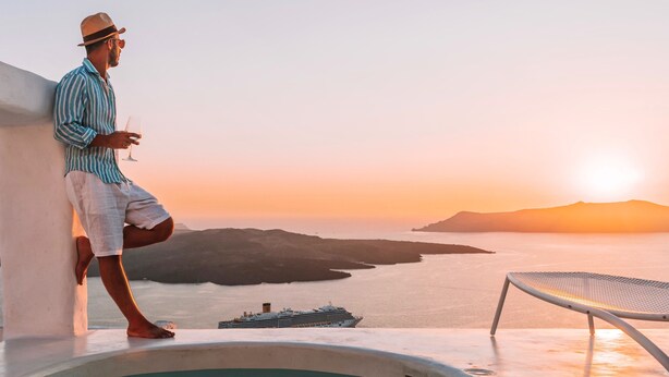 Un homme appuyé contre un mur, près d’une piscine, avec une vue sur le coucher de soleil.