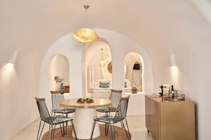 A dining area with a round table, six chairs, and a gold pendant light. - Limestone (Santorini)