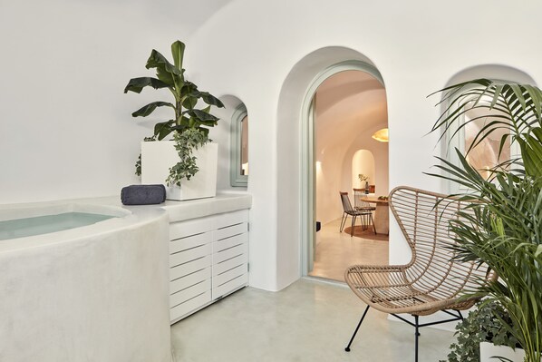 A modern interior with a bathtub, white cabinetry, a wicker chair, and a dining area visible through an archway. - Limestone (Santorini)