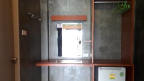 A room with a single window, a door, a small trash bin, and a refrigerator. - SP Resort (Lahan Sai)