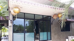 A modern building with large glass doors, a covered entrance area, and a small outdoor seating space. - SP Resort (Lahan Sai)