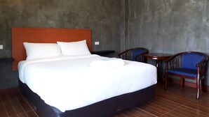 A hotel room with a large bed, two wooden chairs, a small table, and an air conditioning unit. - SP Resort (Lahan Sai)