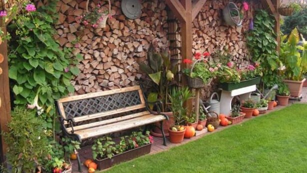 A wooden bench under a pergola with a stone wall behind it, surrounded by potted plants and a neatly trimmed lawn. - Ferienwohnung Kerstin (Siggelkow)
