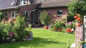 A two-story house with a sloped roof, a front porch, and a well-maintained garden with various flowers and shrubs. - Ferienwohnung Kerstin (Siggelkow)