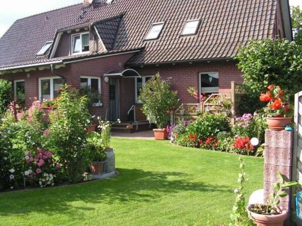A two-story house with a sloped roof, a front porch, and a well-maintained garden with various flowers and shrubs.