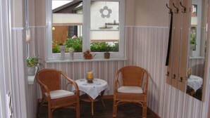 A room with two wicker chairs, a small table with a white tablecloth, and a window with a flower decoration. - Ferienwohnung Kerstin (Siggelkow)