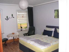 A bedroom with a bed, a chair, a small table, and a window with blinds.