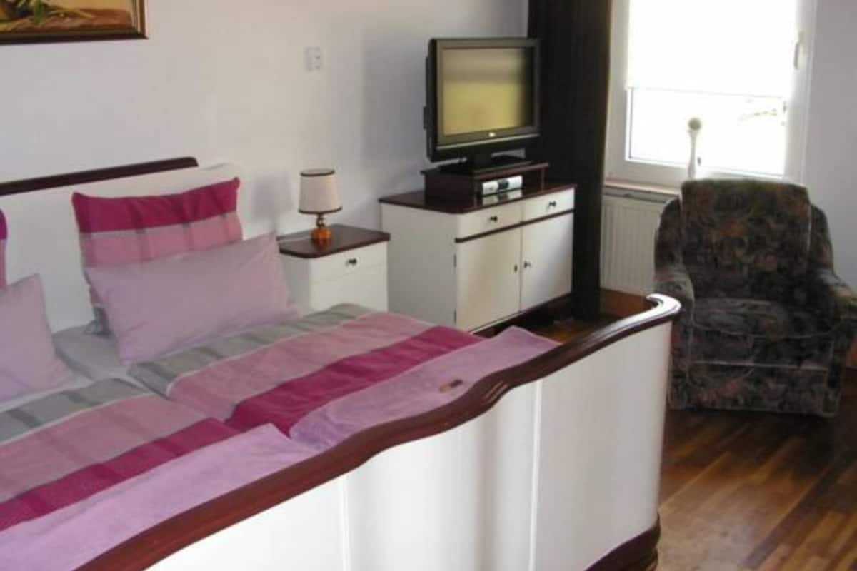 A bedroom with a bed, a television on a stand, a chair, and a window.