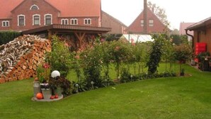 A residential area with a well-maintained lawn, a stack of firewood, and a variety of flowering plants. - Ferienwohnung Kerstin (Siggelkow)