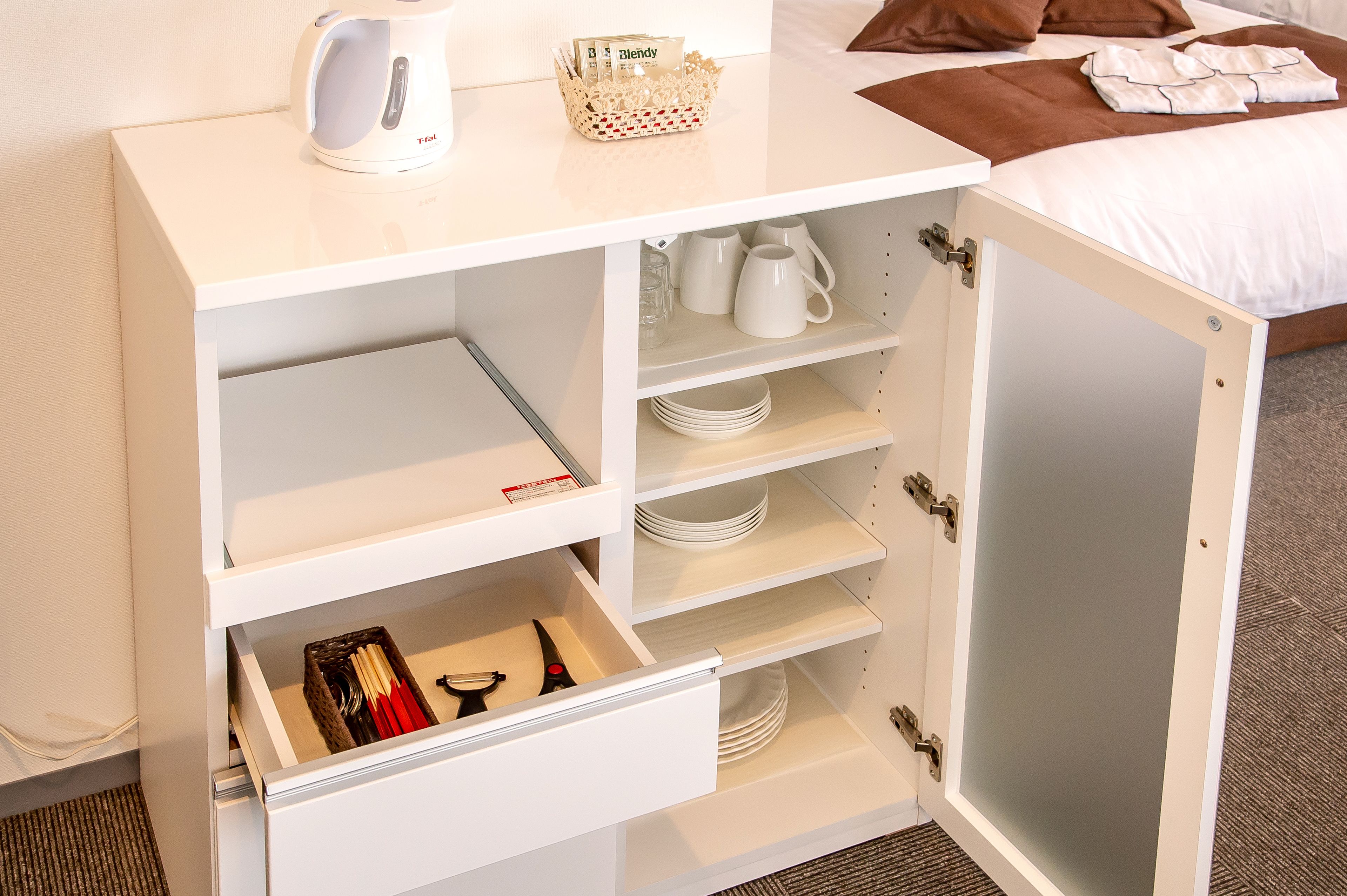 Ein weißer Schrank mit mehreren Regalen und Schubladen, der Geschirr und einen Korb mit Karten enthält.