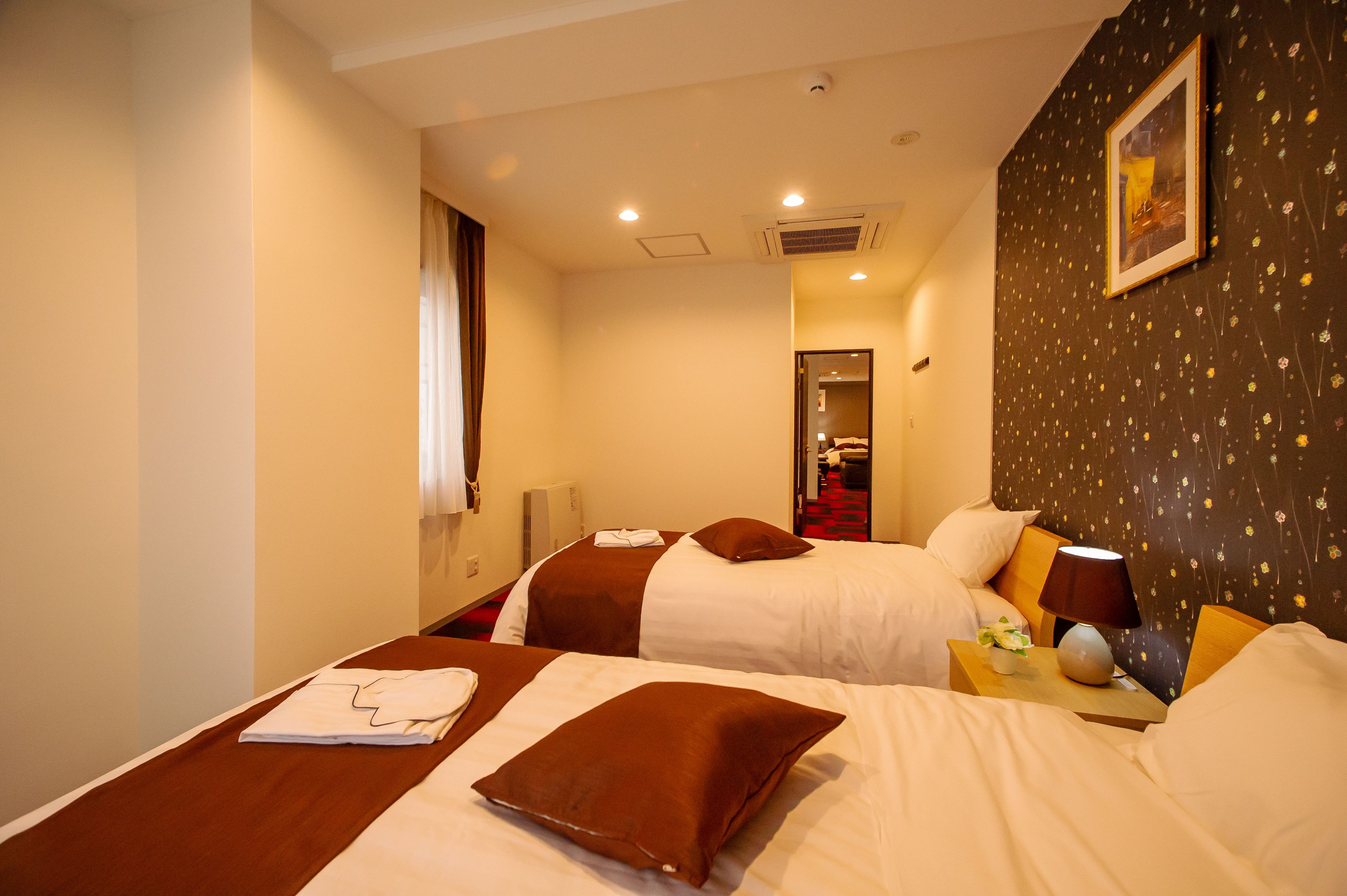 Een hotelkamer met twee bedden, een nachtkastje met een lamp en een ingelijst schilderij aan de muur.