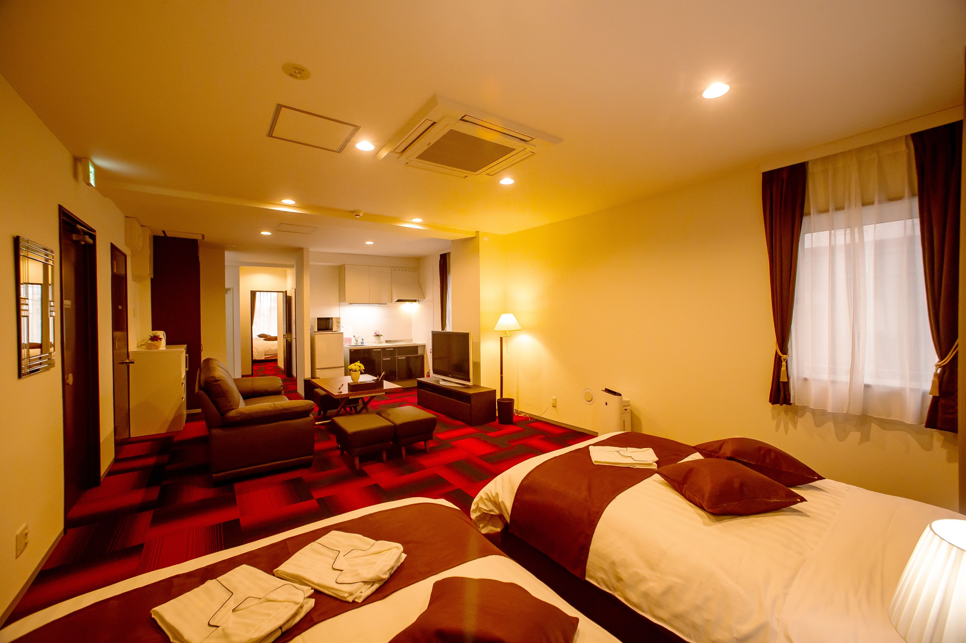 A hotel room with a red carpet, a sofa, a TV, a desk, and a bed.