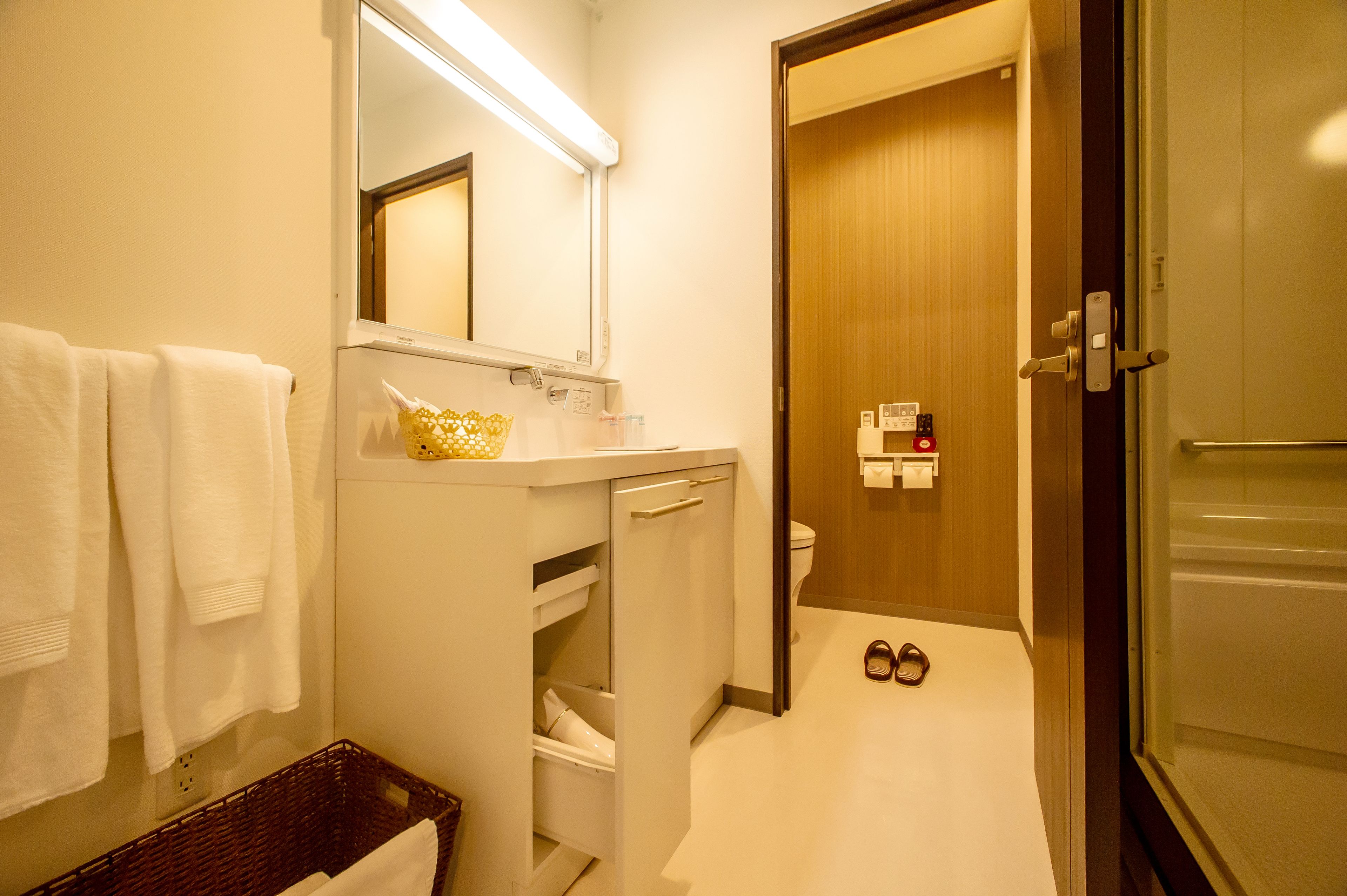 A bathroom with a white sink, mirror, and towel rack. There is a wooden door and a basket on the floor.