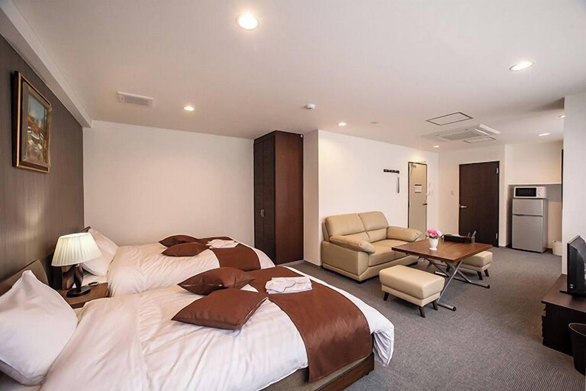 A hotel room with two beds, a sofa, a table, and a TV.