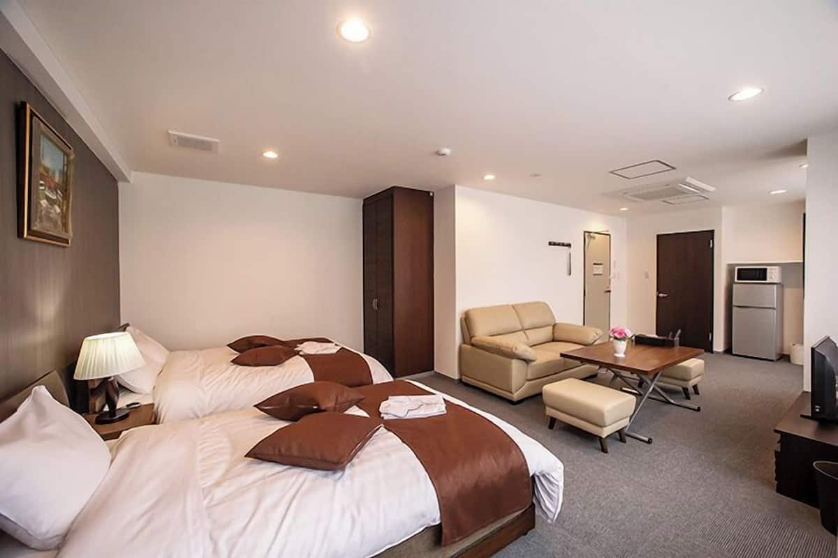 A hotel room with two beds, a sofa, a table, and a TV.