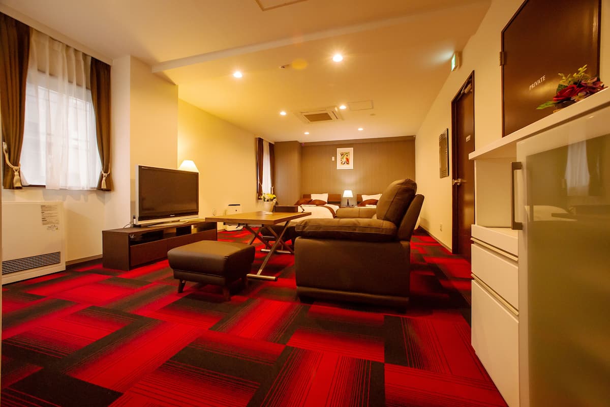 A hotel room with a bed, a sofa, a TV, a desk, and a refrigerator.