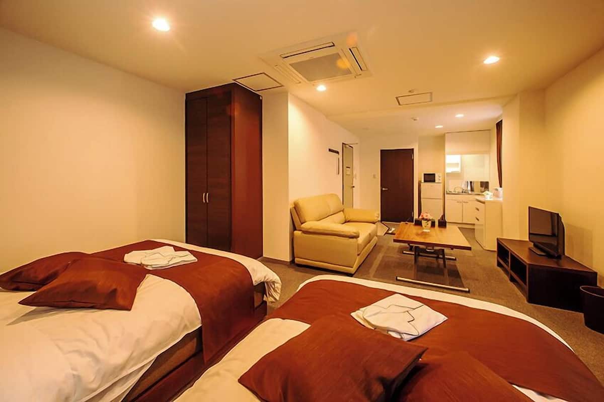 A hotel room with two beds, a sofa, a desk, a TV, and a kitchenette.