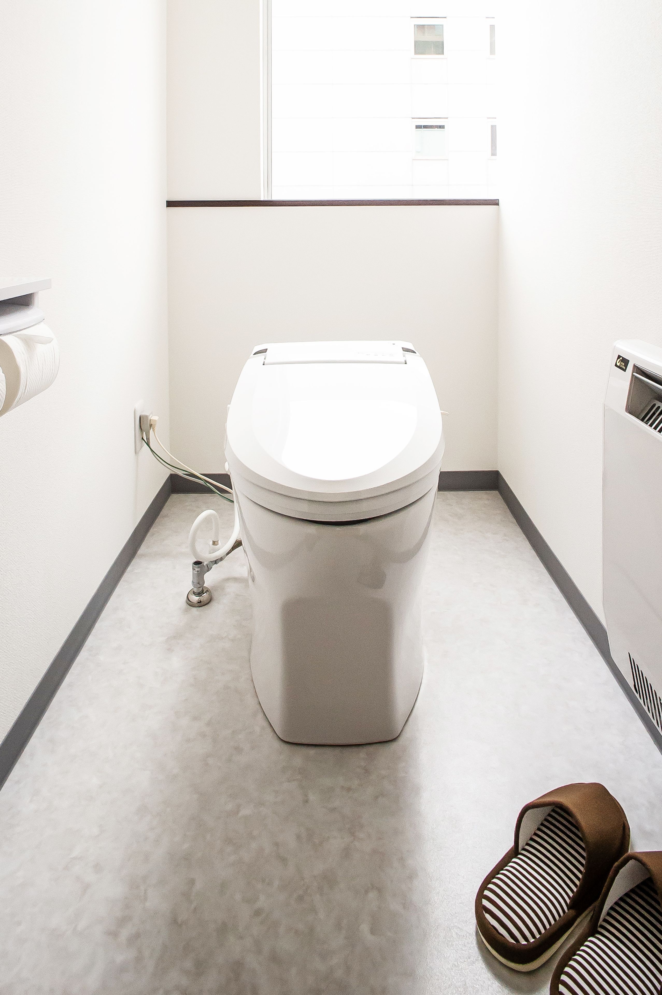 A modern bathroom with a toilet, a hand dryer, and a pair of slippers on the floor.