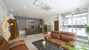A reception area with a receptionist desk, a statue, a brown leather sofa, a black marble table with a vase, and a large window with a view of the street. - Condominium Stella Site (Hakodate)