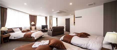 A hotel room with three beds, a sofa, a TV, and a desk with a lamp.