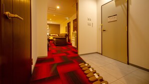 A hotel hallway with a red carpet leading to a seating area with brown chairs. - Condominium Stella Site (Hakodate)