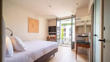 A bedroom with a bed, bedside table, and a TV. There is a balcony with a table and chairs.