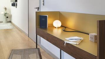 Una habitación de hotel moderna con un escritorio de madera, una lámpara de pie, una obra de arte enmarcada y un televisor montado en la pared.