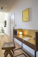 Una habitación de hotel moderna con un escritorio de madera, una lámpara de pie, una obra de arte enmarcada y un televisor montado en la pared.