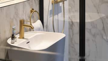 A modern bathroom with a white sink, gold fixtures, and a marble backsplash.