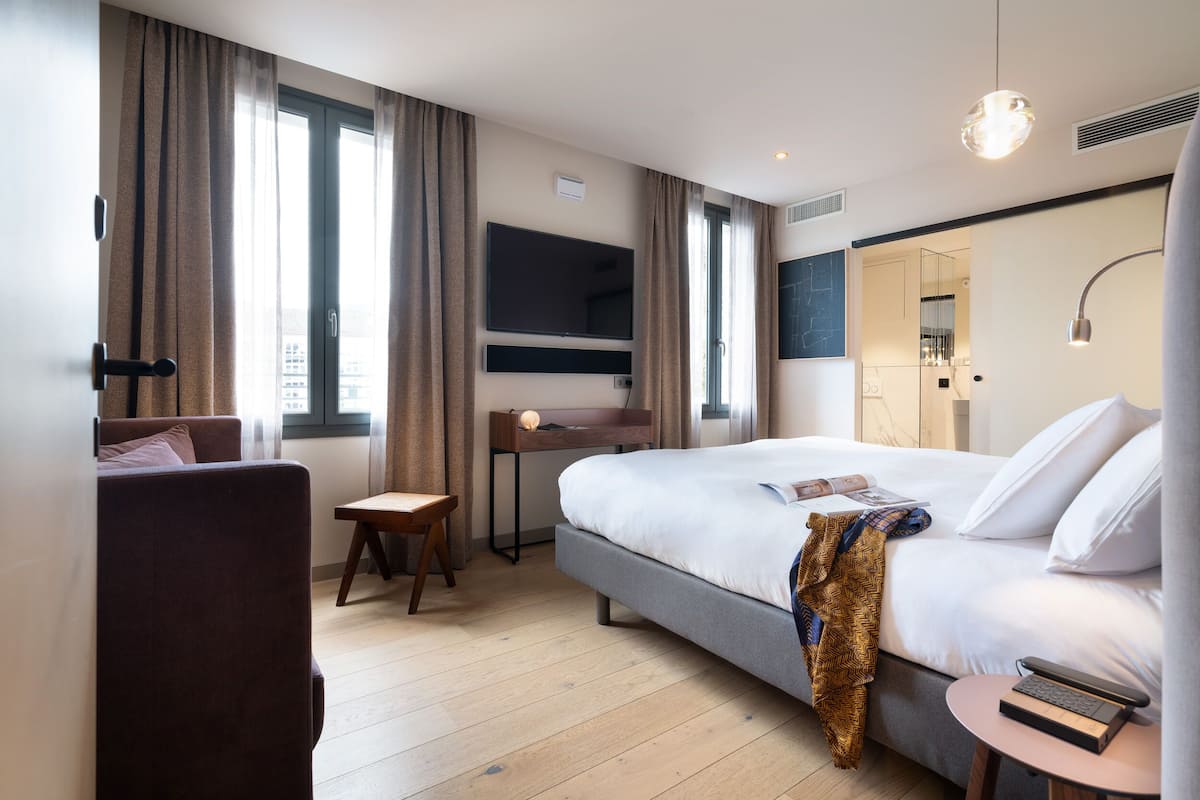 A modern hotel room with a large bed, a desk, a TV, and a bathroom visible through an open door.