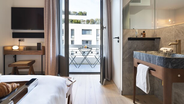 A hotel room with a bed, bedside table, TV, and a balcony with a table and chairs. - Hebe Hotel (Annecy)