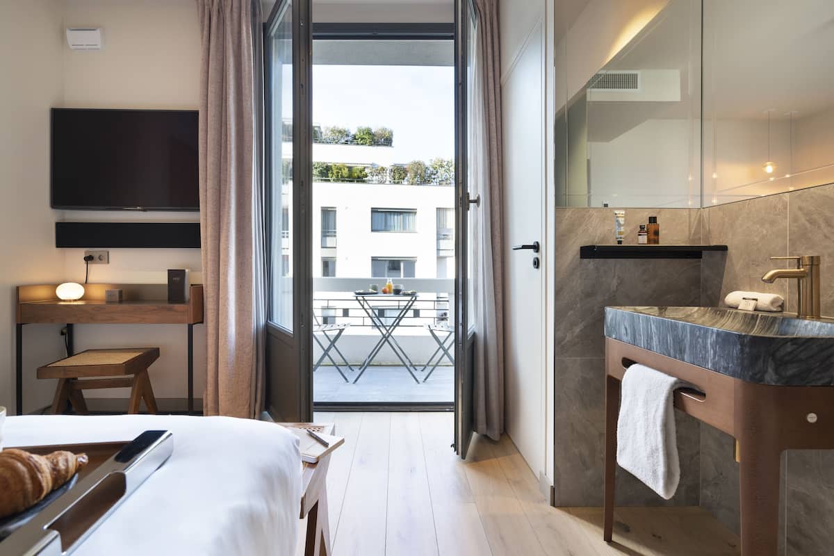 A hotel room with a bed, bedside table, TV, and a balcony with a table and chairs.